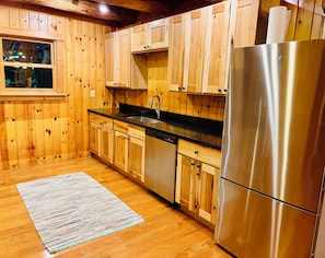 A kitchen with wooden cabinets, a stainless steel refrigerator, a sink, and a window.