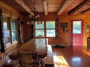 L’intérieur d’un chalet en bois, avec une grande table à manger, des chaises, un lustre et une porte rouge.
