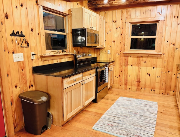 A kitchen with wooden walls, a black countertop, stainless steel appliances, and a trash bin.