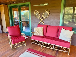 A wooden interior with a red sofa and a wicker chair, a wooden floor, and a green-framed door.