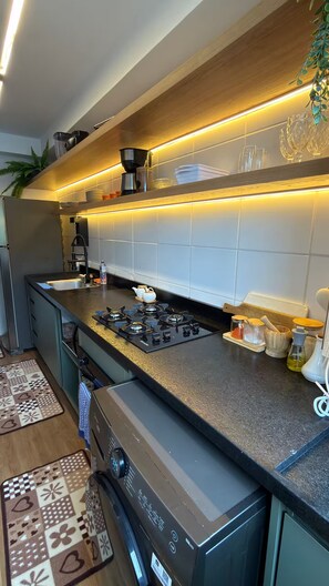 A modern kitchen with a gas stove, a built-in oven, and a stainless steel sink. - Cozy apartment in Barra Olímpica, close to the beaches. (Rio de Janeiro)