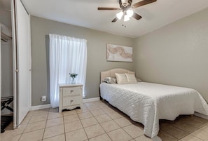 A bedroom with a bed, a nightstand, a ceiling fan, and a window with curtains. - Peaceful & Spacious 4-bedroom house 20min Airport,FortSam & Downtown San Antonio (San Antonio)
