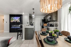 A modern kitchen with a central island, a dining area with a wooden table, and a TV mounted on the wall. - Peaceful & Spacious 4-bedroom house 20min Airport,FortSam & Downtown San Antonio (San Antonio)