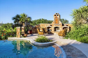 Una piscina con borde de piedra, un edificio de piedra con torre y mobiliario exterior.
