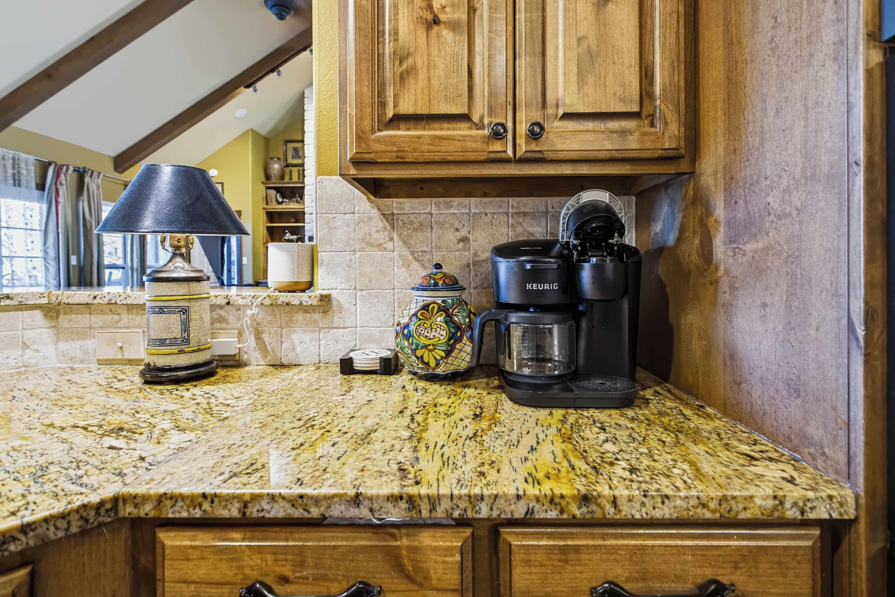 A kitchen with a coffee maker, a clock, and a lamp on a granite countertop.