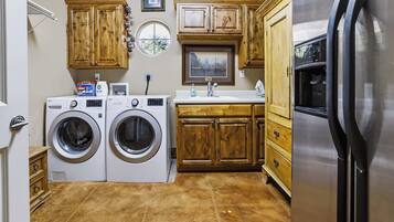 A laundry room with two front-loading washing machines, wooden cabinets, a sink, and a refrigerator.