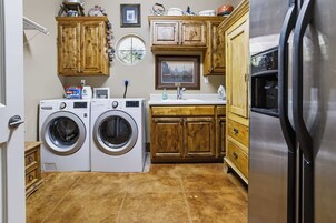 Un lavadero con dos lavadoras de carga frontal, armarios de madera, un lavamanos y un refrigerador.