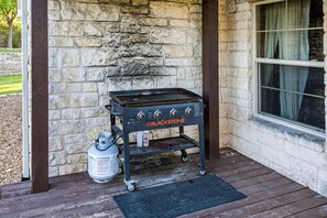 A portable Blackstone grill with controls, a propane tank, and a metal cart on a wooden deck. - Luna Vista With Private Pool Oasis (Kerrville)