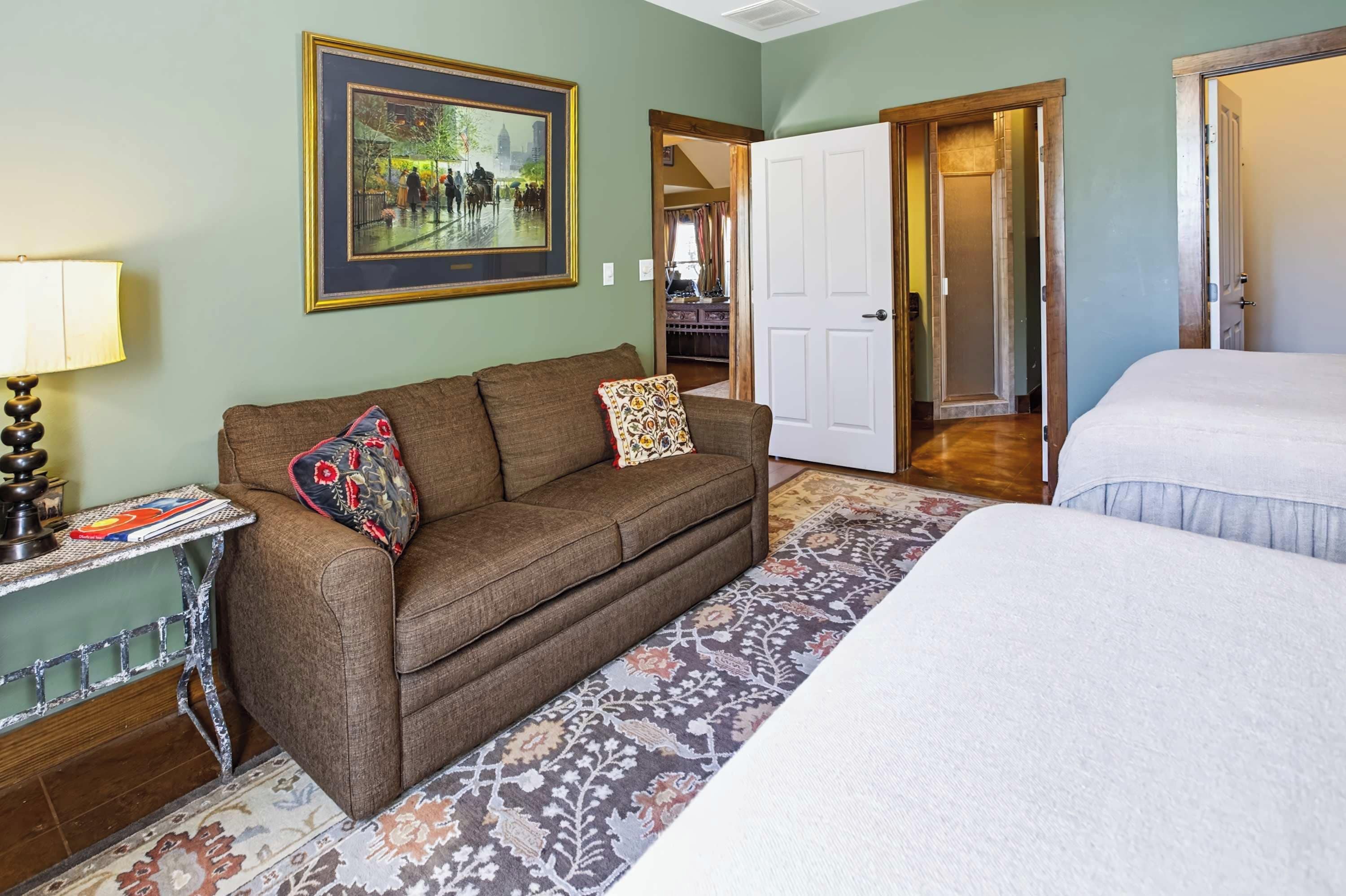 A room with a brown sofa, a bed, a framed picture on the wall, and a door leading to another room.