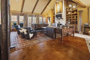 A spacious living room with a high ceiling, a fireplace, and a large window with curtains. - Luna Vista With Private Pool Oasis (Kerrville)