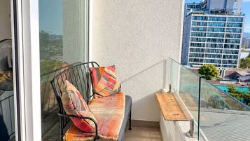A balcony with a metal chair, cushions, and a glass railing overlooking a cityscape.