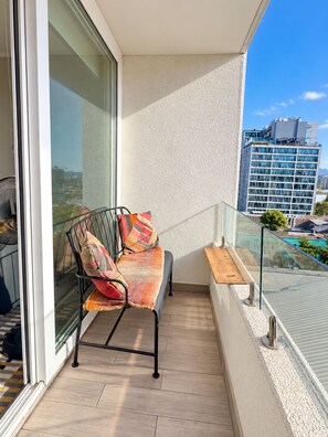 A balcony with a metal chair, cushions, and a glass railing overlooking a cityscape. - AC - Estadio Nacional - Estacionamiento (Ñuñoa)