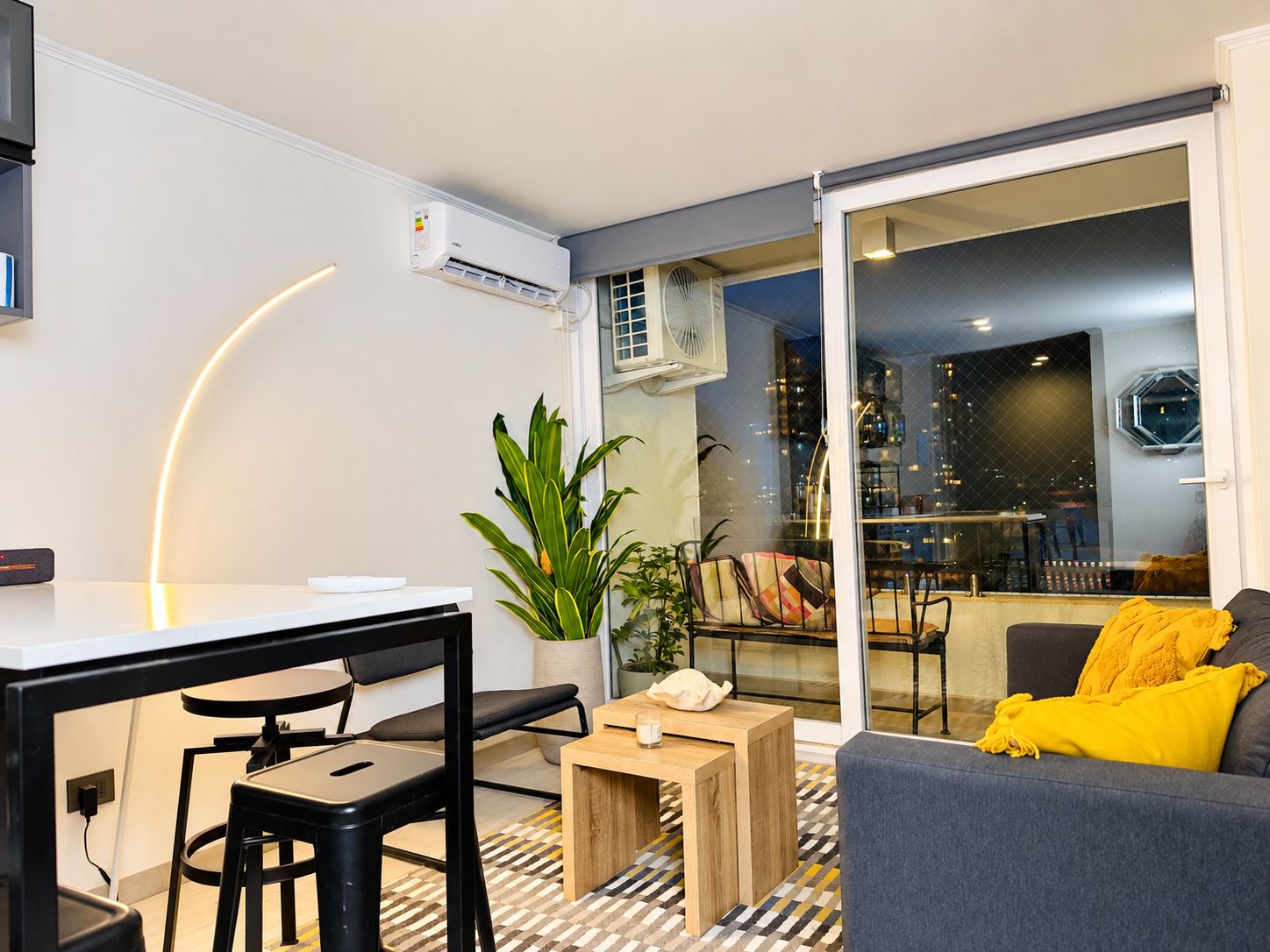 A modern living space with a dining area, a sofa, and a view of the cityscape through a glass door.