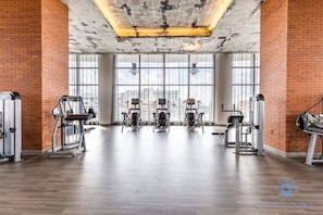 A spacious gym with various exercise machines, large windows, and a high ceiling. - Luxurious Resort 2BD - Resort Bay Corner Views (Hollywood)