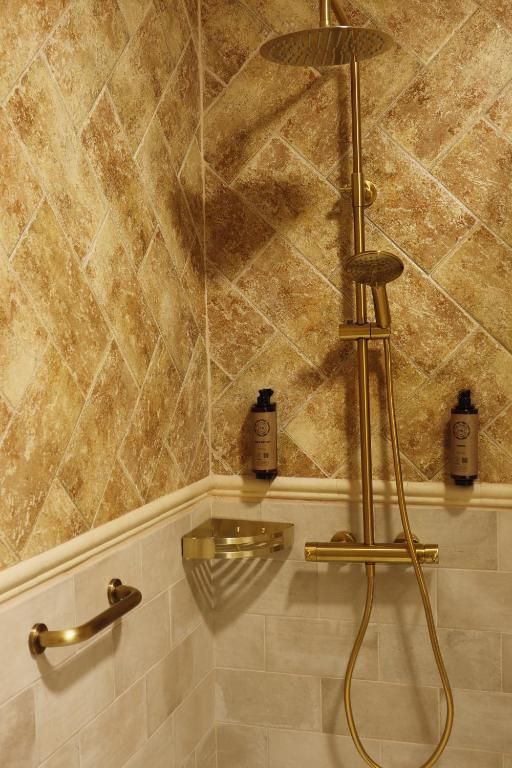 Una ducha con cabezal y panel de control dorados, frente a una pared de azulejos con diseño de rombos.