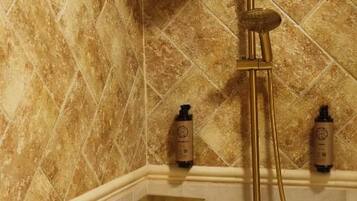 Una ducha con cabezal y panel de control dorados, frente a una pared de azulejos con diseño de rombos.