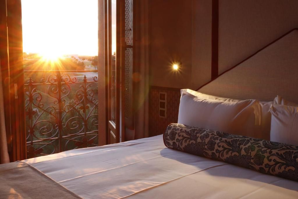 A hotel room with a bed, a view of the outside, and a balcony with decorative iron railings.