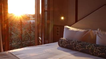 A hotel room with a bed, a view of the outside, and a balcony with decorative iron railings.