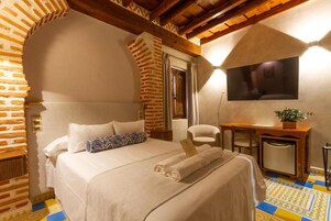 Habitación de hotel con pared de ladrillo, cama con ropa blanca, escritorio con silla y televisor montado en la pared.