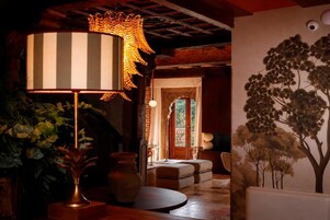 Una habitación con una lámpara grande a rayas, un florero y un mural en la pared con un motivo de árboles.