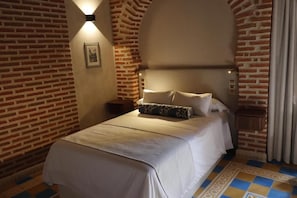 A hotel room with a brick wall, a bed with white bedding, a nightstand, and a picture on the wall.