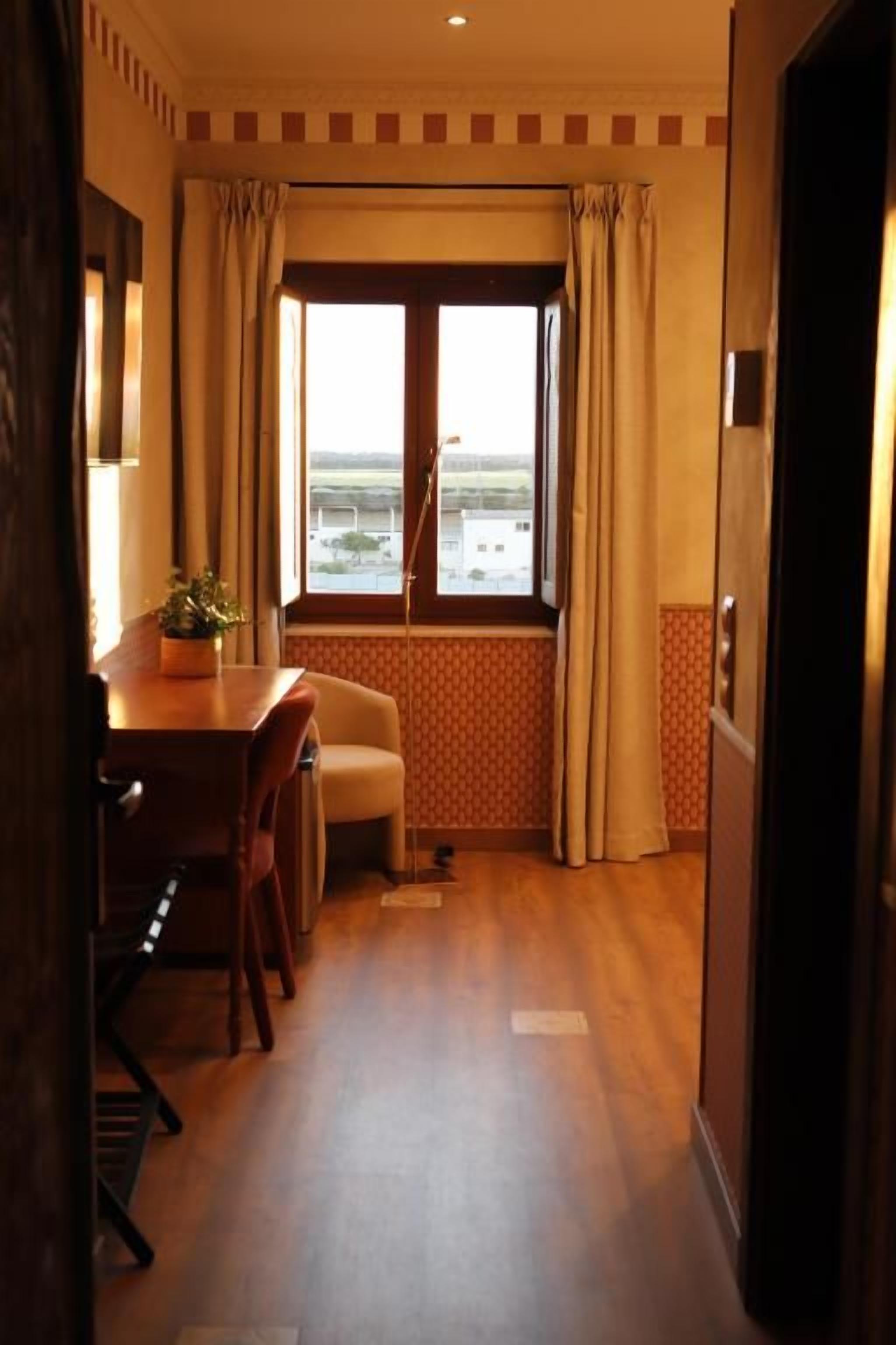 Una habitación de hotel con zona de comedor, ventana con cortinas y vistas al exterior.