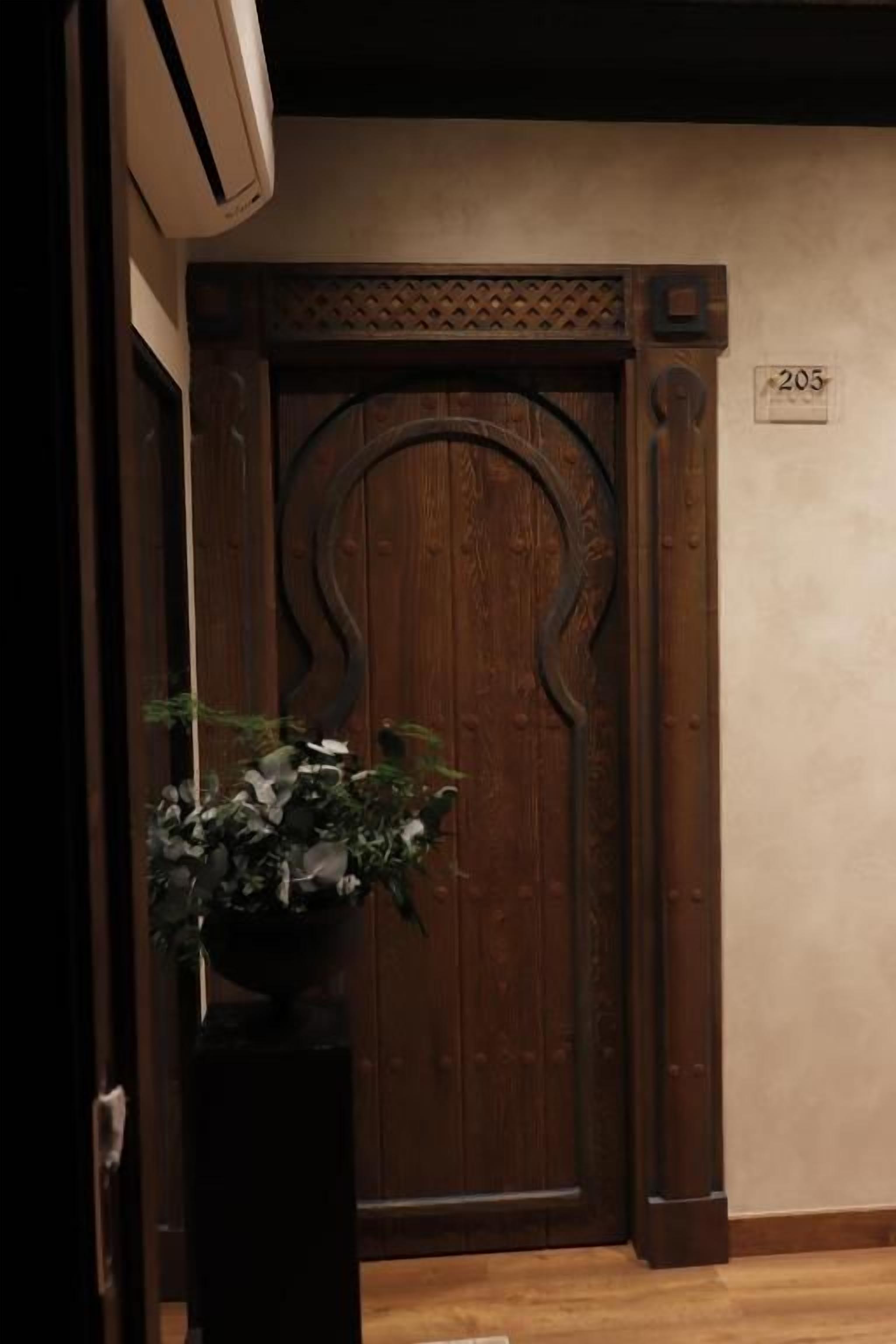 A wooden door with a number '203' above it, a potted plant to the left, and a wall-mounted air conditioning unit above.