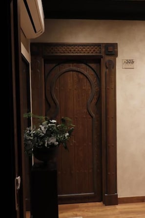 A wooden door with a number '203' above it, a potted plant to the left, and a wall-mounted air conditioning unit above.