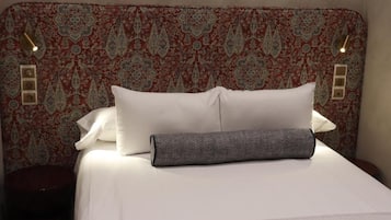 A bed with a patterned headboard, white bedding, and a gray pillow.