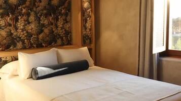 Una habitación de hotel con una cama grande, papel tapiz floral, una ventana con cortinas y una lámpara fijada a la pared.