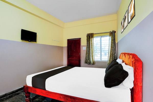 A room with a bed, a television mounted on the wall, a window with curtains, and a door.