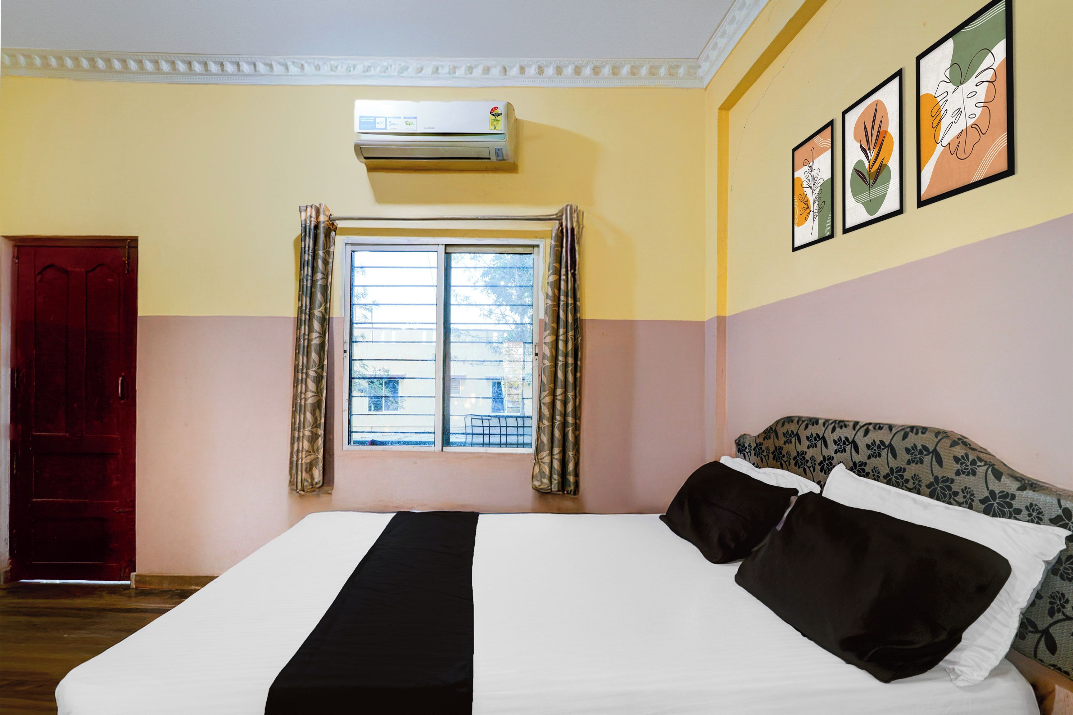 A hotel room with a bed, a window with curtains, an air conditioning unit, and wall art.