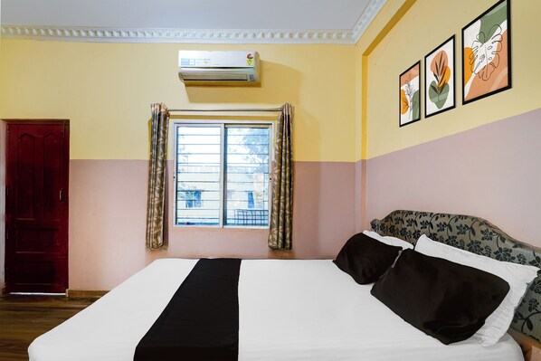 Une chambre d’hôtel avec un lit, une fenêtre avec des rideaux, un appareil de climatisation et des œuvres d’art murales.