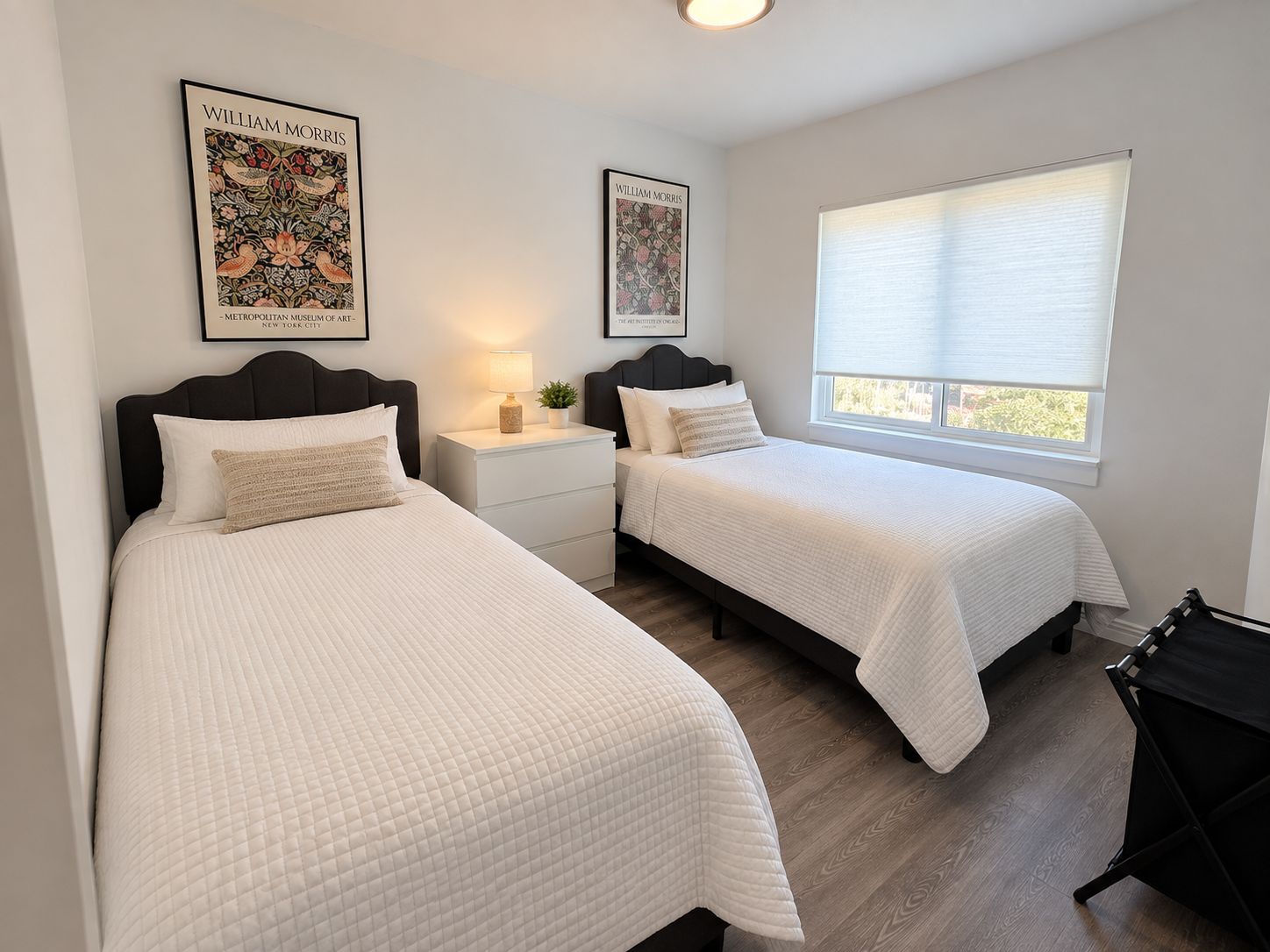Une chambre avec deux lits, une table de chevet avec une lampe et deux tableaux encadrés au mur.