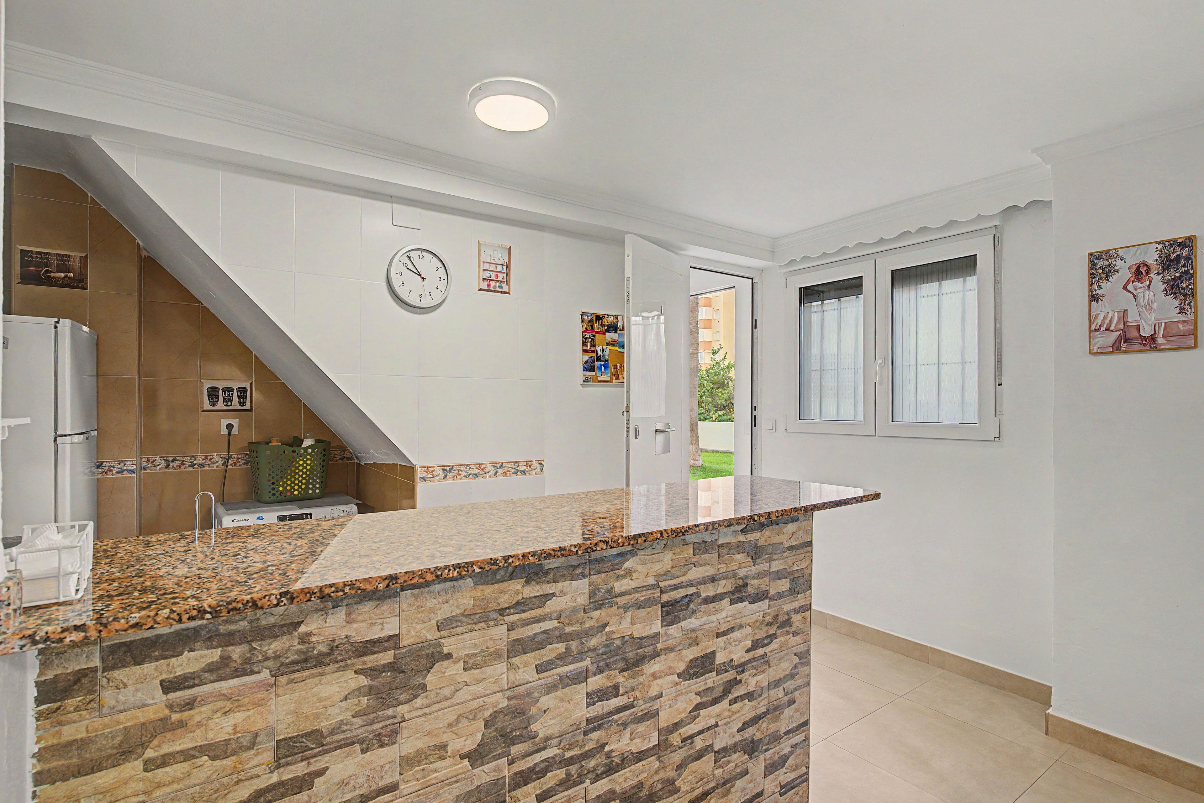 A kitchen with a stone countertop, a clock, and a door leading to a balcony.