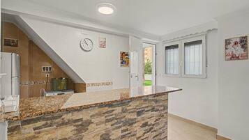 A kitchen with a stone countertop, a clock, and a door leading to a balcony.