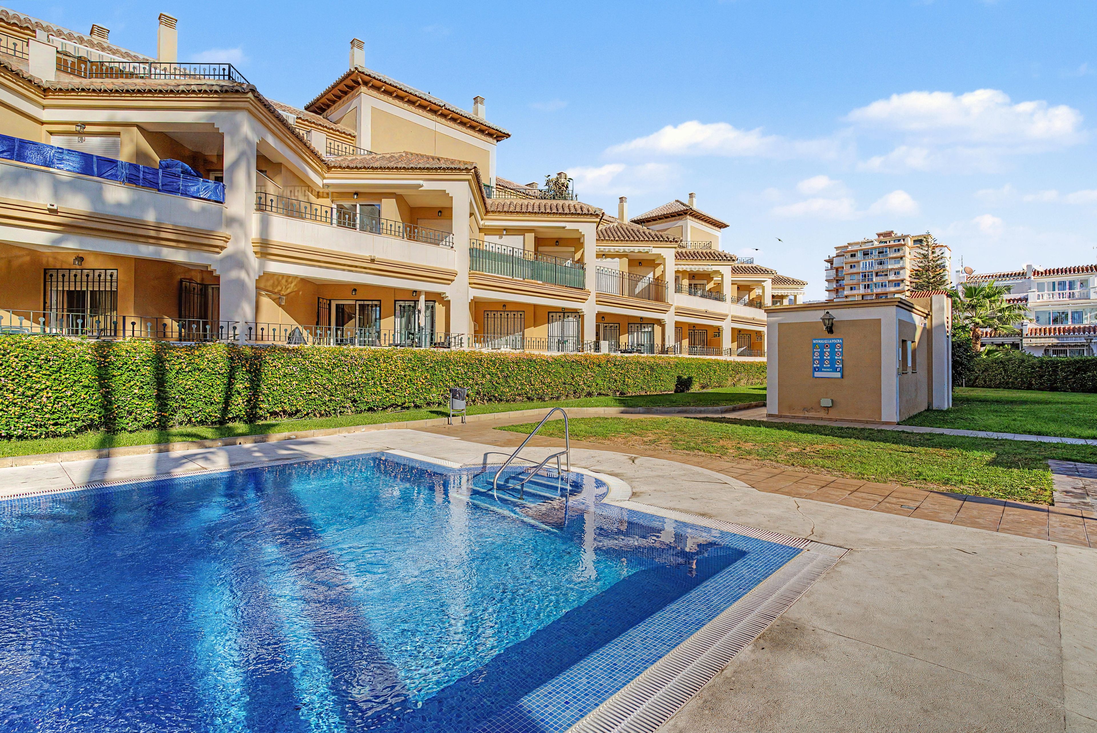 A residential building with a swimming pool, balconies, and a small garden area.