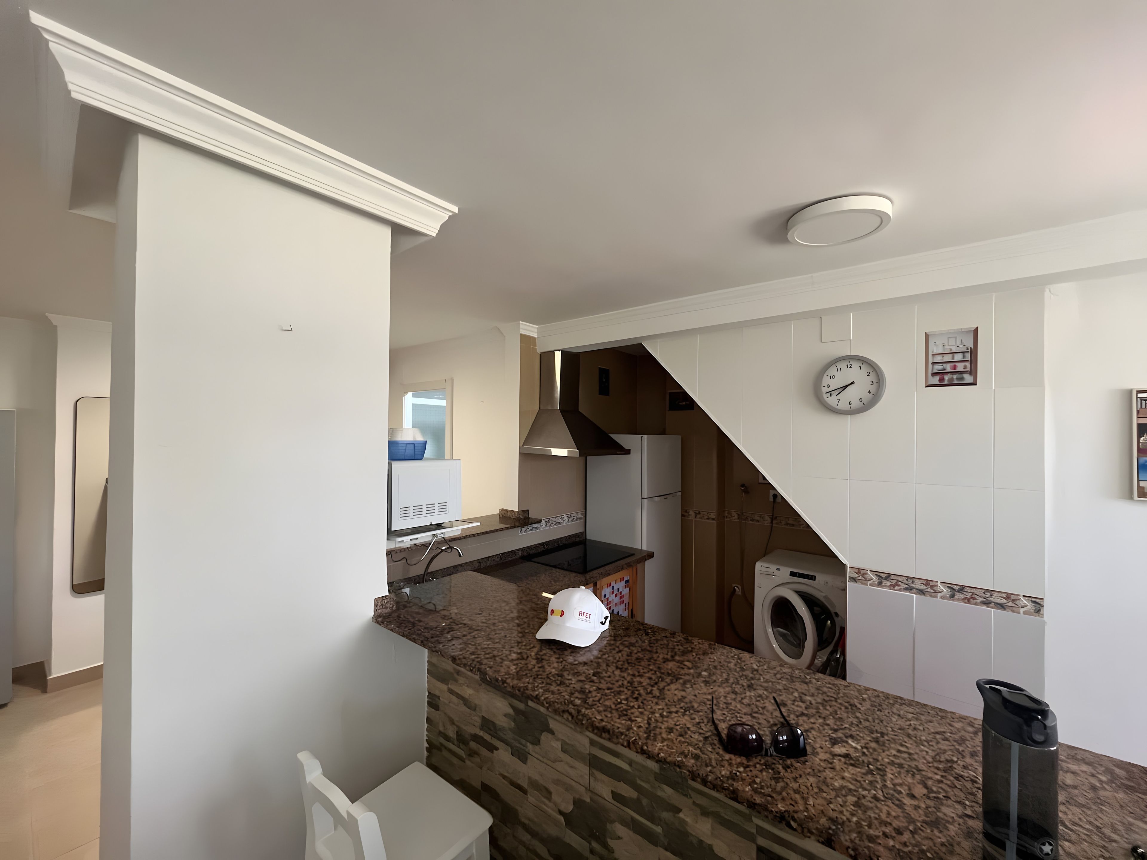 A kitchen with a granite countertop, a built-in oven, a microwave, and a washing machine.