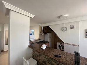 A kitchen with a granite countertop, a built-in oven, a microwave, and a washing machine.