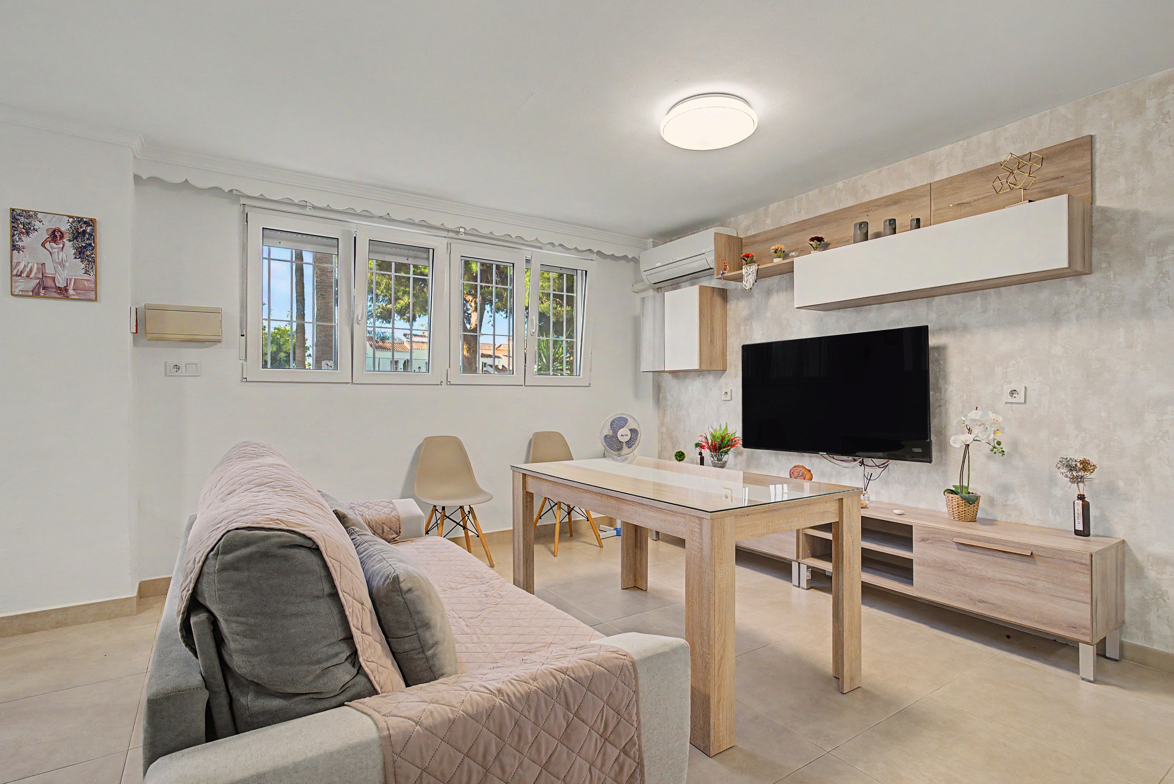 Een moderne woonkamer met een bank, een eettafel, stoelen, een televisie en een wandairconditioning.