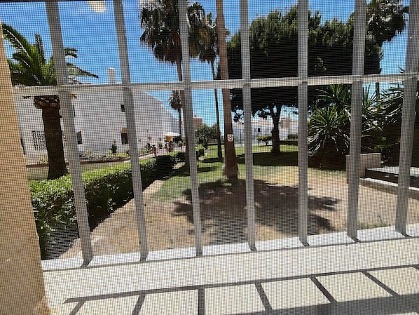 A view through a window with a grid pattern, featuring outdoor seating areas, trees, and a clear sky.