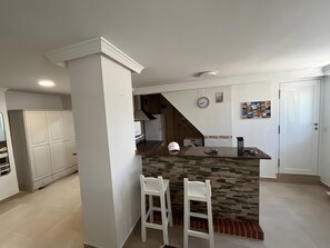 A kitchen with a stone countertop, two white bar stools, a white wardrobe, and a white door.