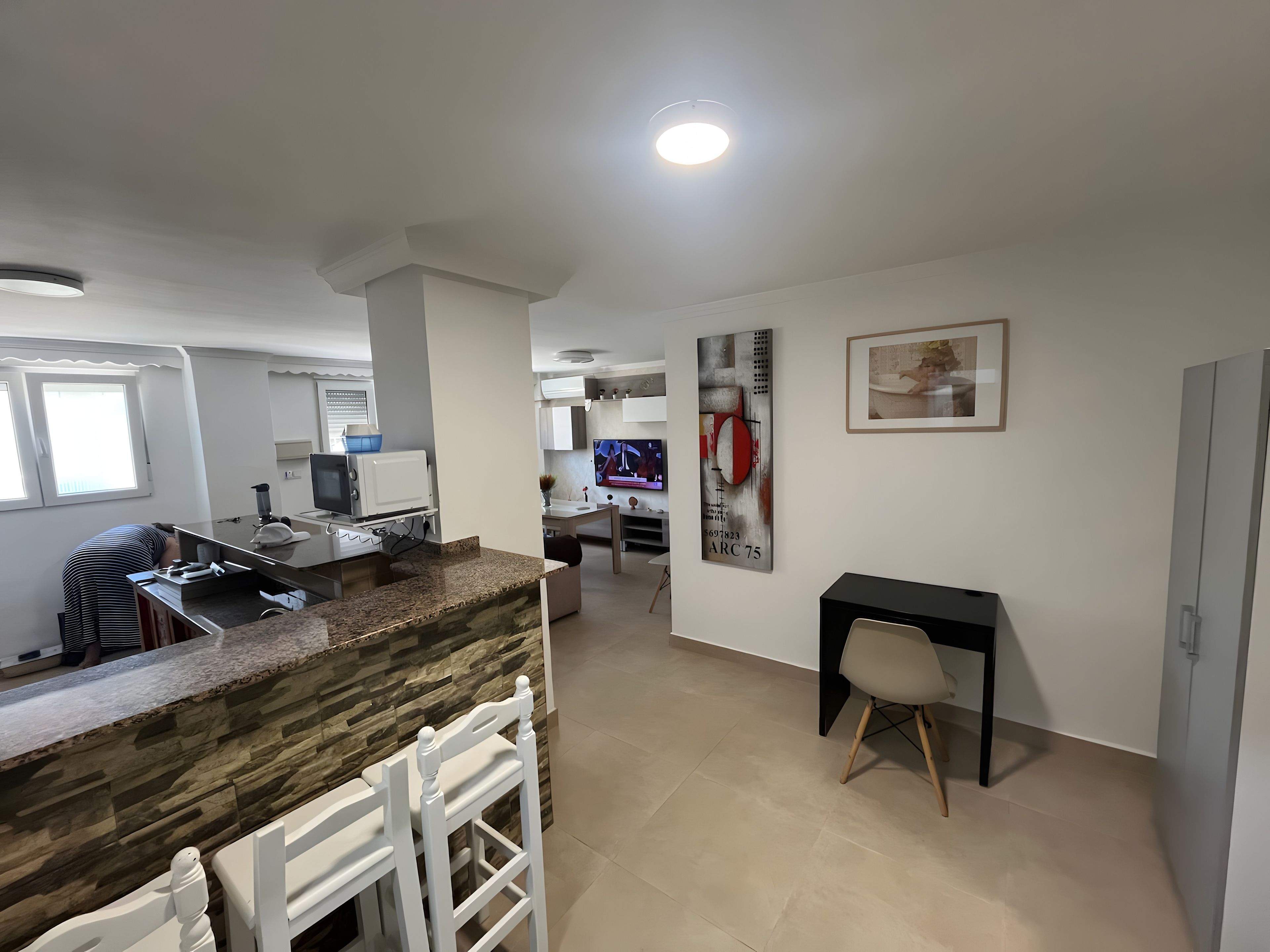 Una cocina moderna con encimeras de granito, armarios blancos y un comedor con una silla blanca.