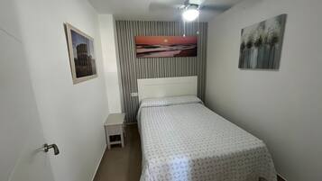 A bedroom with a bed, a nightstand, a ceiling fan, a wall-mounted air conditioner, and a framed picture.