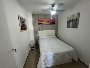 A bedroom with a bed, a nightstand, a ceiling fan, a wall-mounted air conditioner, and a framed picture.