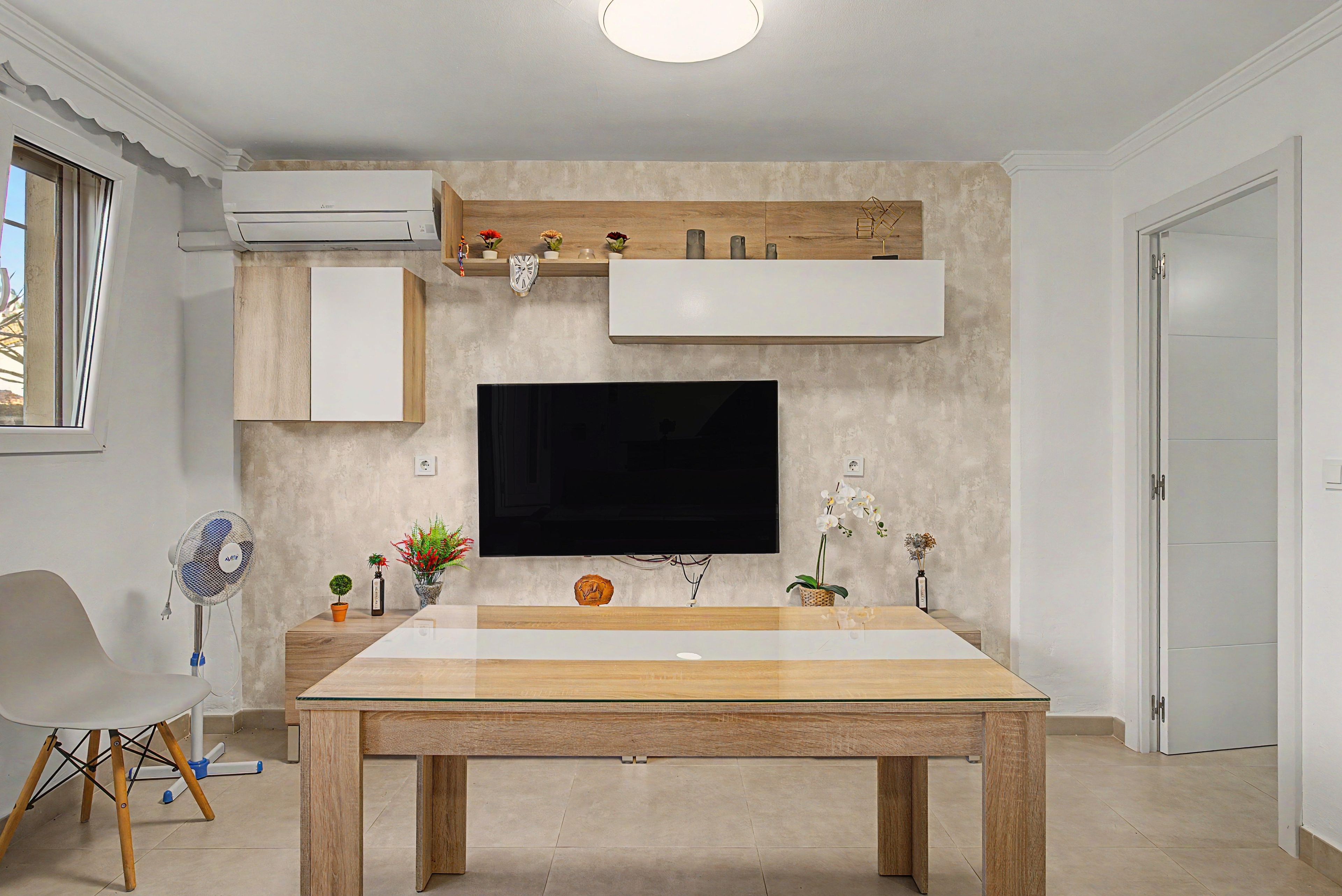 Un soggiorno moderno con una TV a schermo piatto montata su una parete strutturata, un tavolo da pranzo in legno e un tavolino con oggetti decorativi.