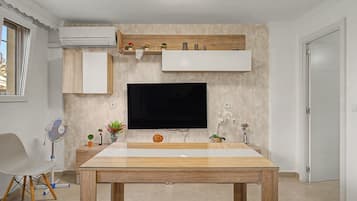 Un soggiorno moderno con una TV a schermo piatto montata su una parete strutturata, un tavolo da pranzo in legno e un tavolino con oggetti decorativi.