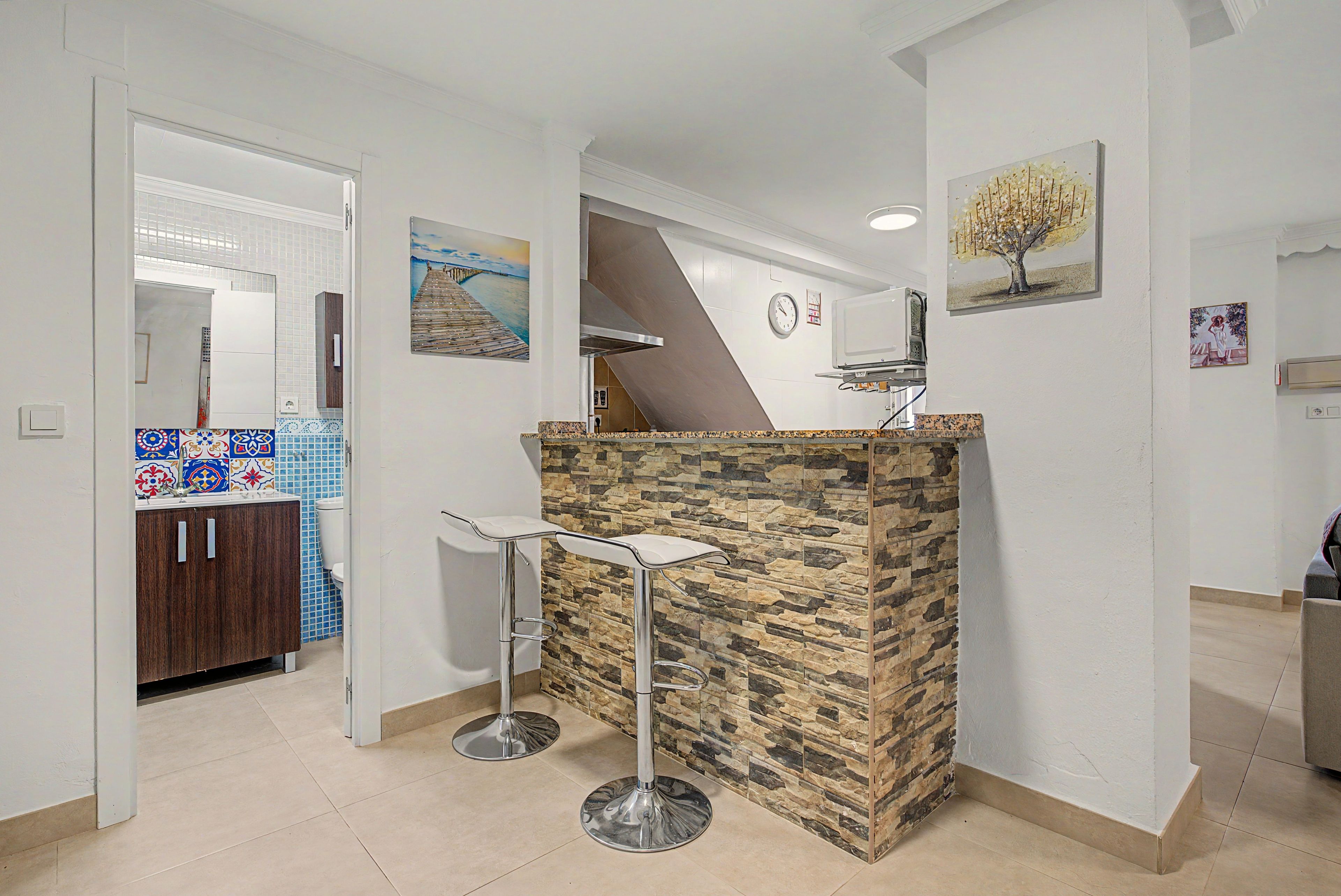 Una cucina moderna con zoccolo in pietra, forno a microonde integrato e angolo bar con sgabelli.