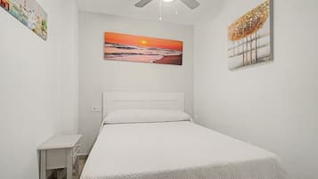 Ein Schlafzimmer mit einem Bett, einem Deckenventilator, einem Sonnenuntergangsbild und einem kleinen Nachttisch.