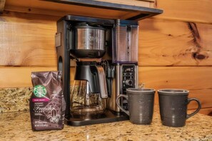 Eine Kaffeemaschine, eine Packung Starbucks French Roast Kaffee und zwei Tassen auf einer Küchenarbeitsplatte.